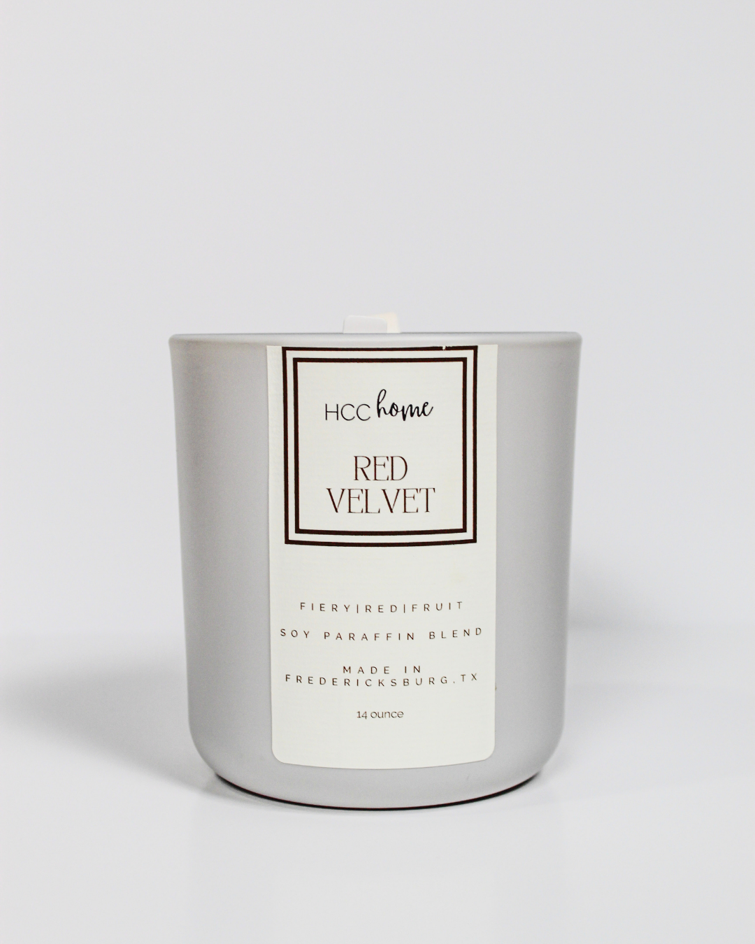 A silver, hand poured candle labeled “HCC Home Candle - Red Velvet” by Hill Country Chocolate, crafted in Fredericksburg, TX with a soy-paraffin blend, sits against a plain white background. This Texas-made candle fills your home with the sweet aroma of red velvet cake.