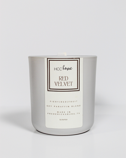 A silver, hand poured candle labeled “HCC Home Candle - Red Velvet” by Hill Country Chocolate, crafted in Fredericksburg, TX with a soy-paraffin blend, sits against a plain white background. This Texas-made candle fills your home with the sweet aroma of red velvet cake.