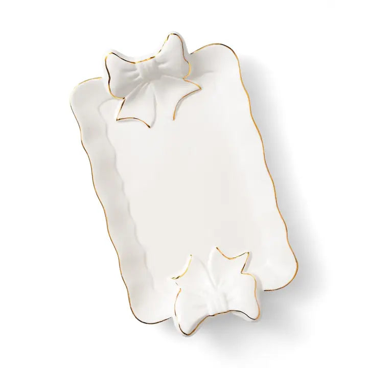 The Hill Country Chocolate Ceramic Platter with Bow is a rectangular white ceramic serving piece with gold trim and two raised bow designs at the top and bottom edges, perfect for charcuterie presentations or as an elegant hostess gift. Shown here on a white background.