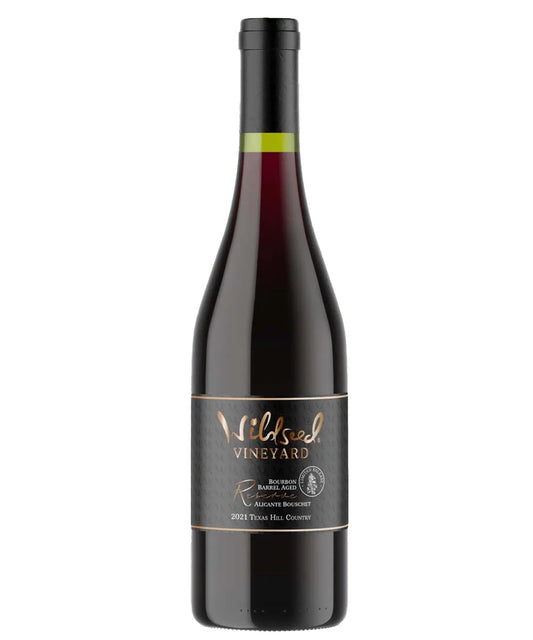 A bottle of 2021 Bourbon Barrel Alicante Bouchet from Wildseed Vineyard by Hill Country Chocolate, a bold red wine with a black label and gold accents.