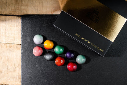 A set of Hill Country Chocolate's 9 piece Signature Artisanal Bonbon Collection on a black table.