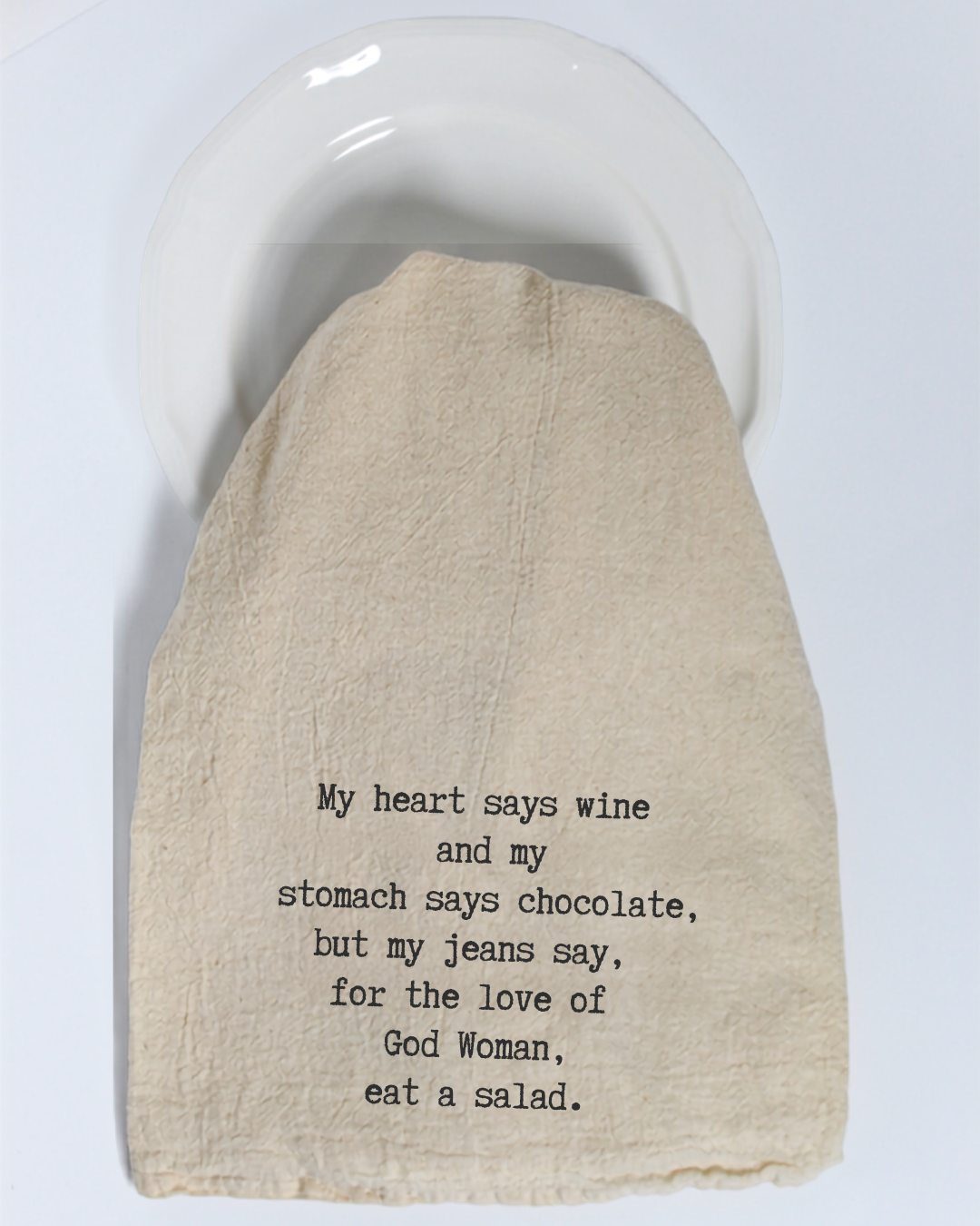 The “My heart says wine and my stomach...” Tea Towel by Hill Country Chocolate features the humorous message: “My heart says wine and my stomach says chocolate, but my jeans say, for the love of God Woman, eat a salad.” Made from natural cotton in a classic beige color, this playful yet practical kitchen towel adds both style and fun to your home décor. Displayed here on a white plate, it makes a charming statement for any kitchen.