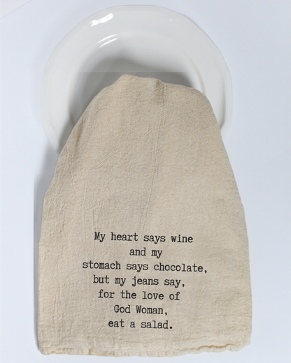 The “My heart says wine and my stomach...” Tea Towel by Hill Country Chocolate features the humorous message: “My heart says wine and my stomach says chocolate, but my jeans say, for the love of God Woman, eat a salad.” Made from natural cotton in a classic beige color, this playful yet practical kitchen towel adds both style and fun to your home décor. Displayed here on a white plate, it makes a charming statement for any kitchen.