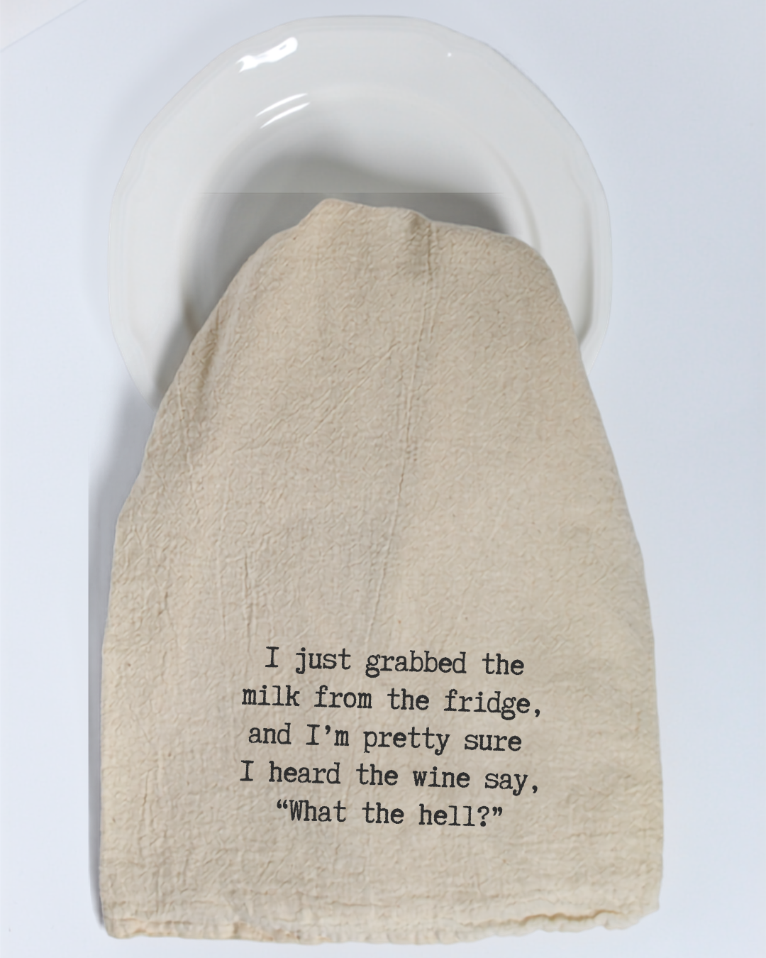 A white plate is partially covered by the Hill Country Chocolate “I just grabbed the milk from the fridge...” tea towel—a funny, eco-friendly cotton kitchen towel that’s perfect for anyone who enjoys a good laugh in the kitchen.