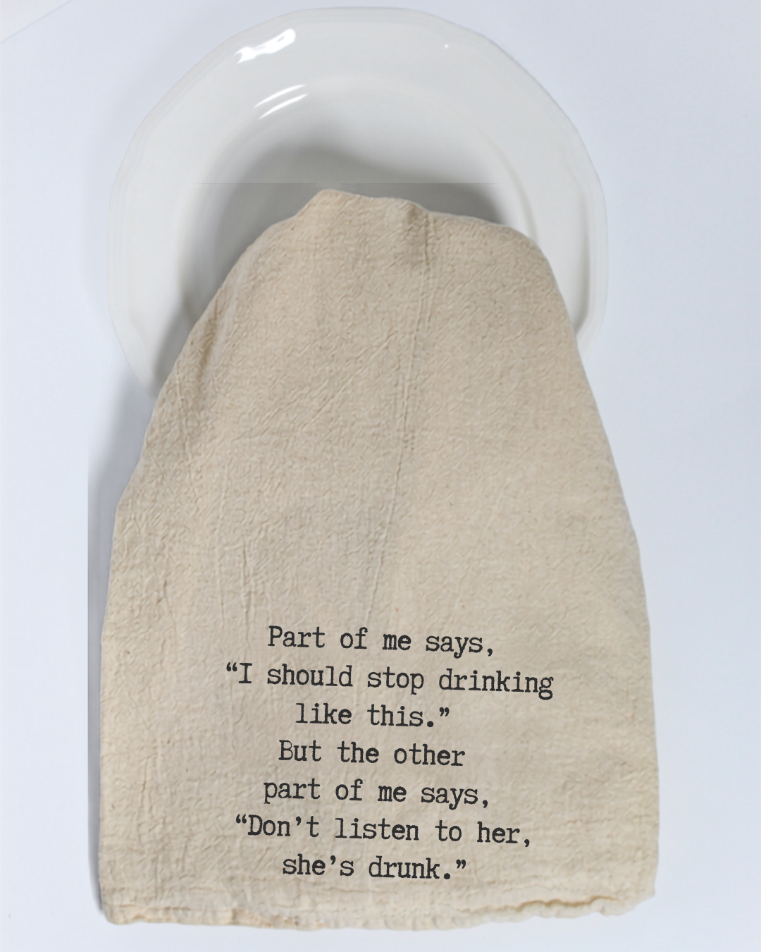 A beige “Part of me says...” eco-friendly tea towel from Hill Country Chocolate, featuring black humorous text about the dilemma between drinking and being drunk, covers a white plate.
