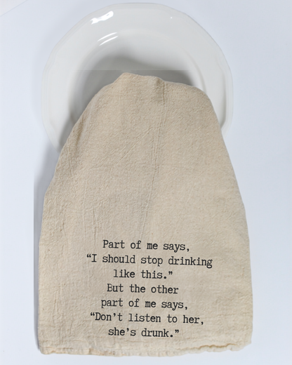 A beige “Part of me says...” eco-friendly tea towel from Hill Country Chocolate, featuring black humorous text about the dilemma between drinking and being drunk, covers a white plate.