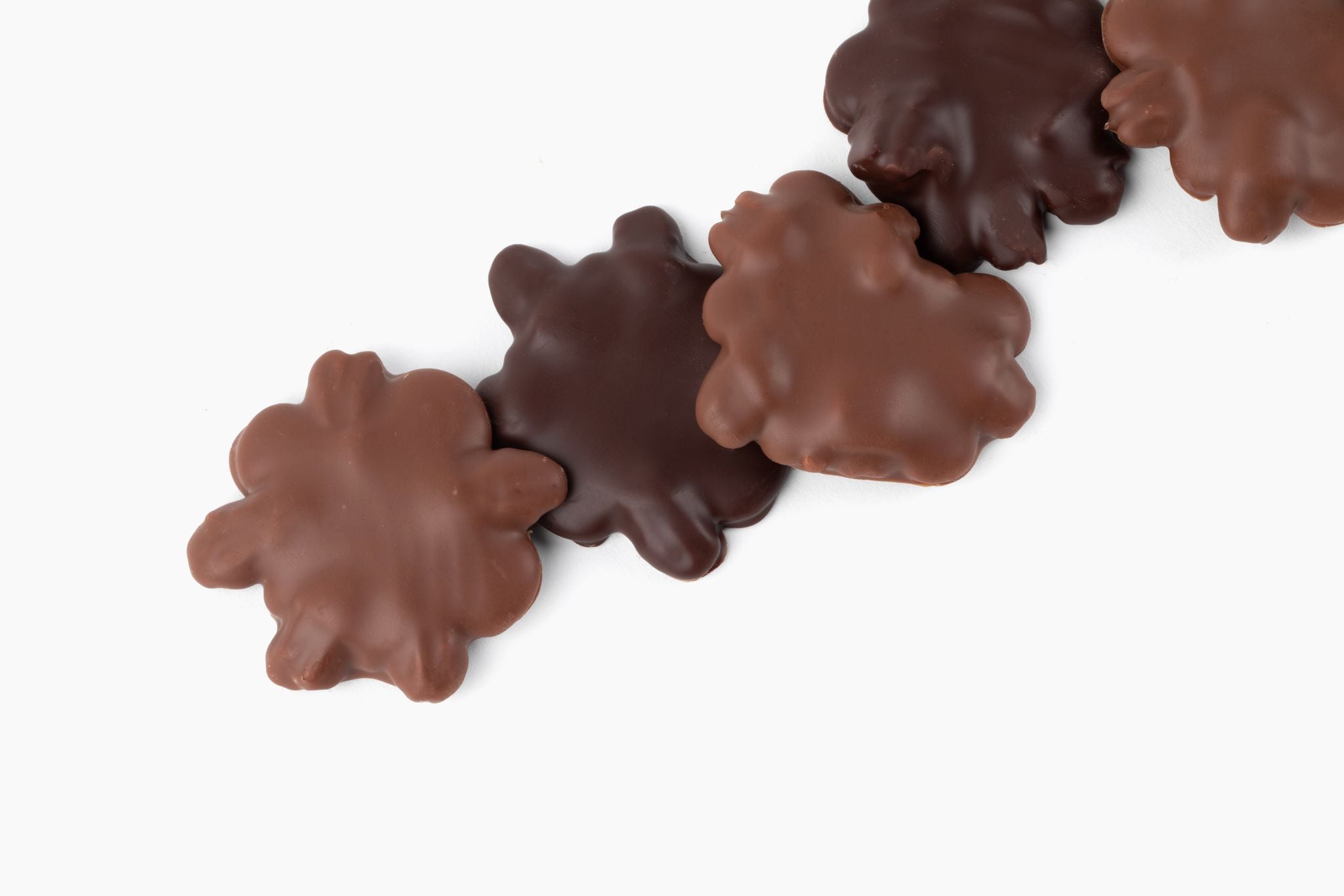 Five pecan clusters covered in milk and dark chocolate arranged in a line on a white background.